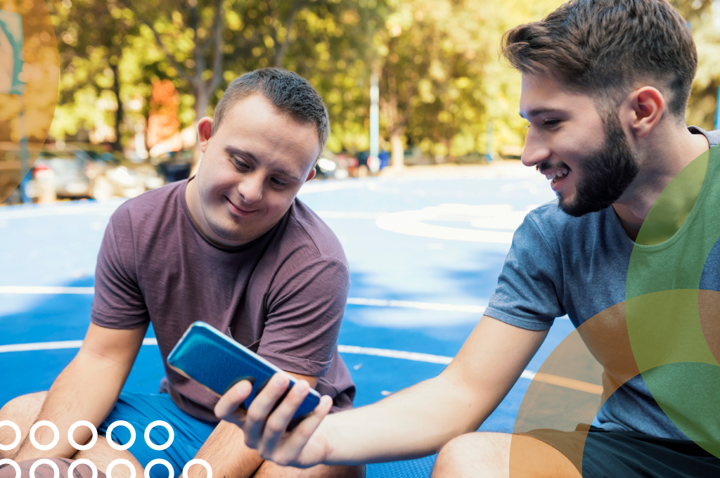 Two men sitting together on basketball court looking at phone